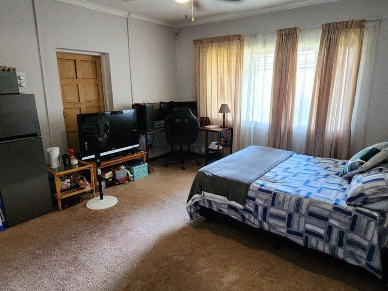 A functional bedroom featuring carpeted flooring, a ceiling fan, and natural light through large windows.