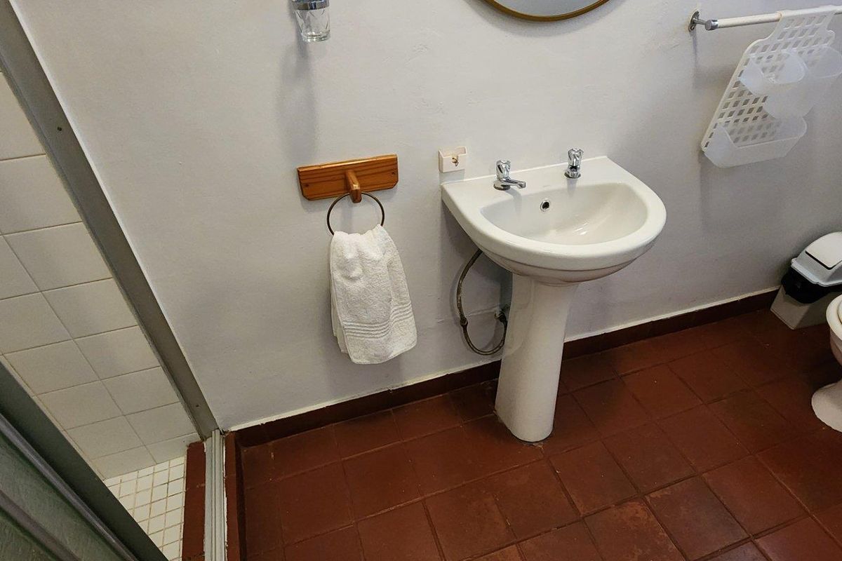 A functional bathroom featuring a pedestal basin, toilet, and a tiled shower enclosure with terracotta-style floor tiles.