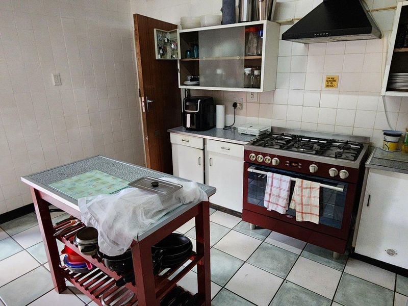 A functional kitchen featuring a gas stove, extractor fan, tiled backsplash, and built-in cabinetry with tiled flooring.