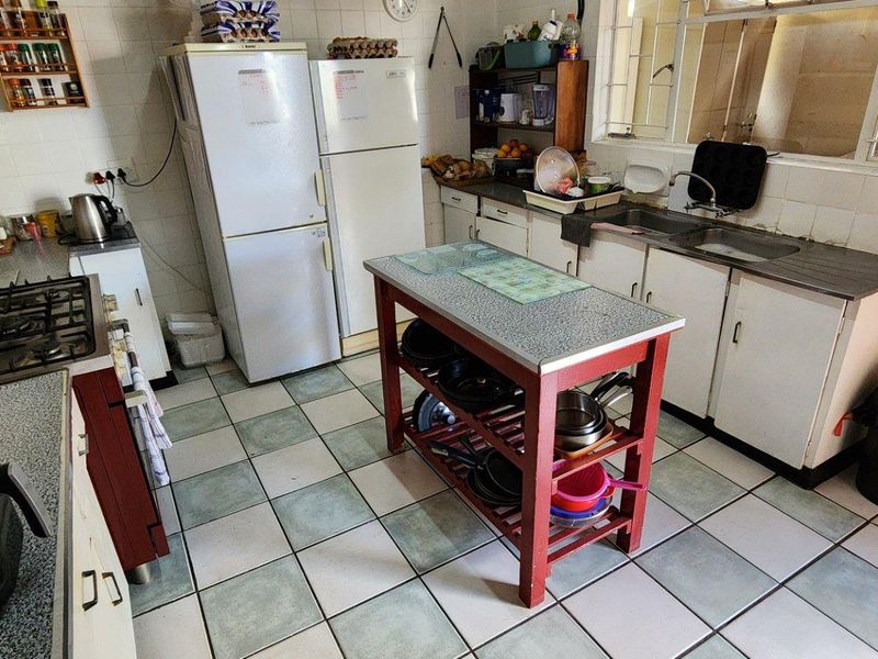 A functional kitchen featuring a gas hob, double basin sink, tiled splashbacks, and ample built-in cabinetry with a central prep island.