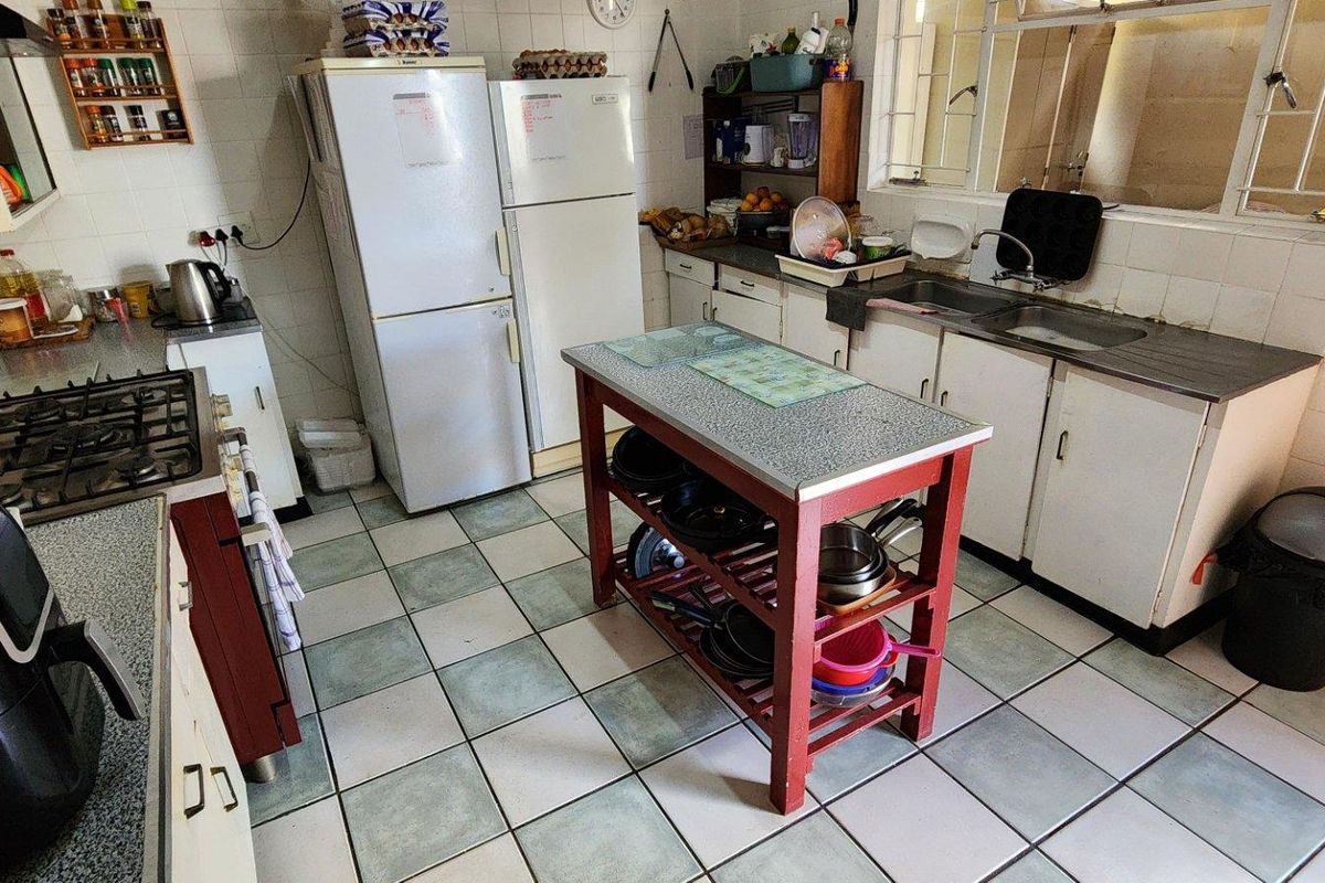 A functional kitchen featuring a gas hob, double basin sink, tiled splashbacks, and ample built-in cabinetry with a central prep island.