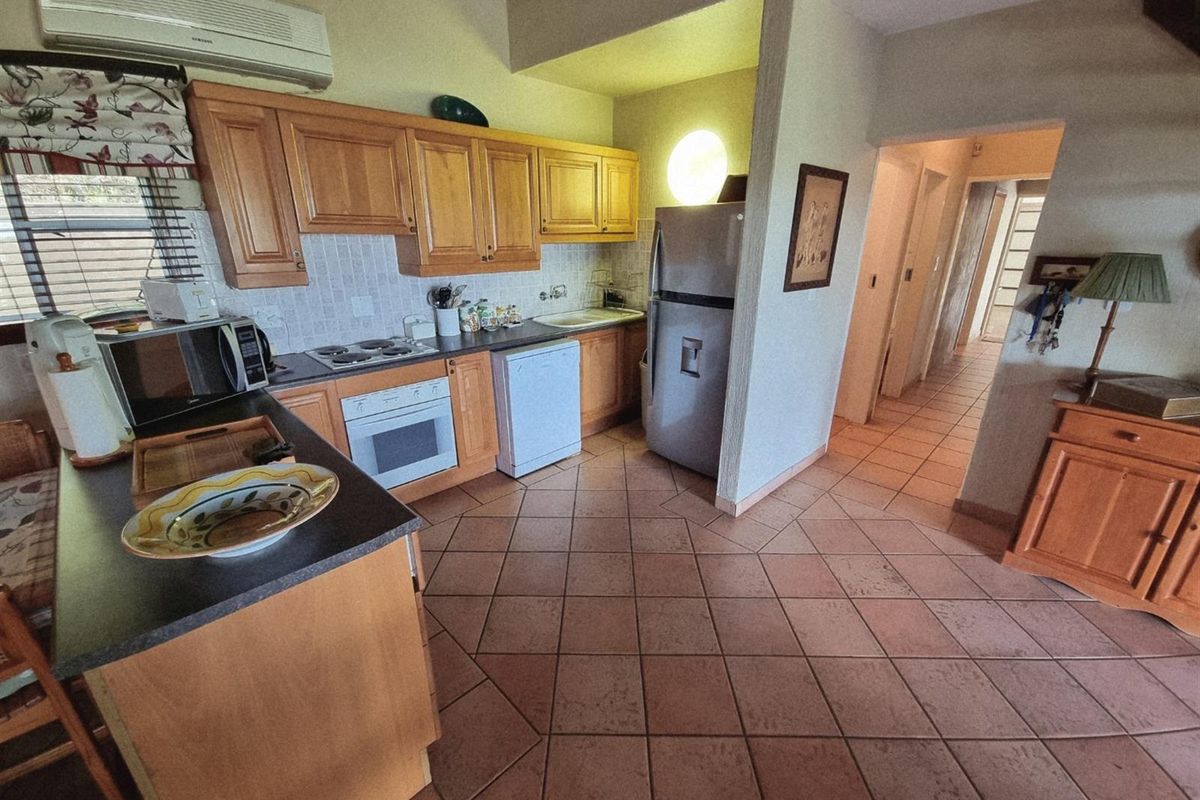A functional kitchen featuring wooden cabinetry, tiled flooring, and integrated appliances, leading into a hallway area.