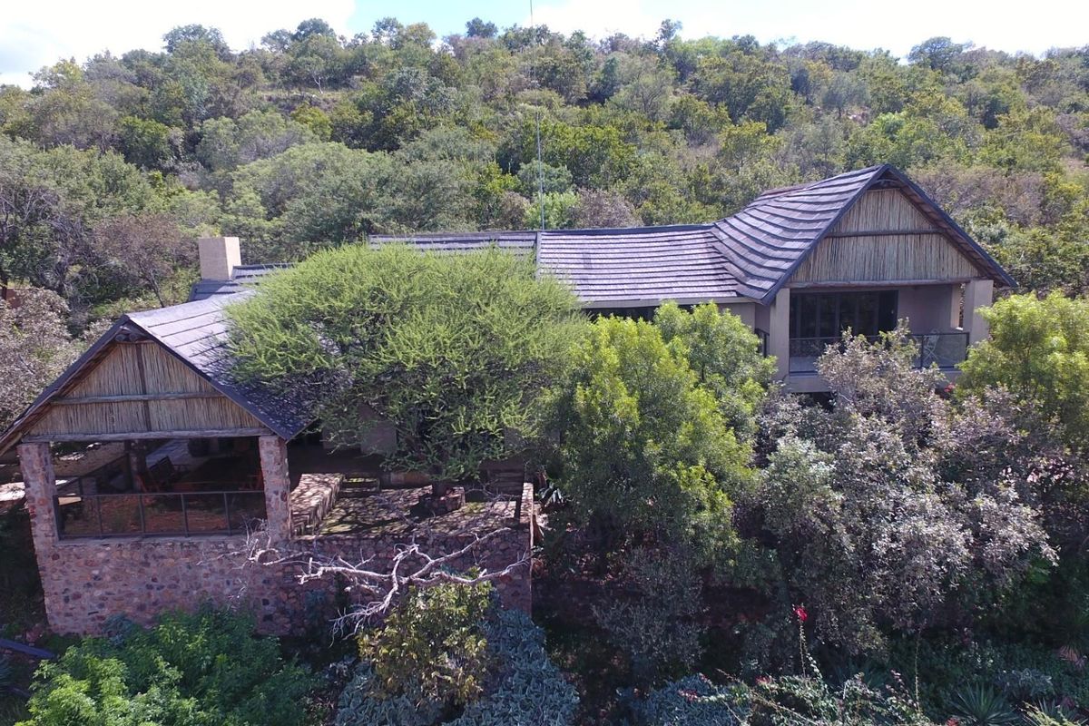Aerial view of a farm-style residence featuring stone masonry, thatched roof sections, and a covered patio nestled within a lush, wooded landscape.