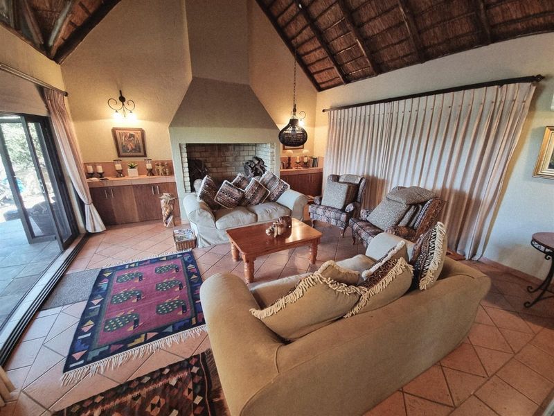 Spacious living room featuring a high vaulted thatched ceiling, large brick fireplace, and sliding glass doors leading to the outdoor area.