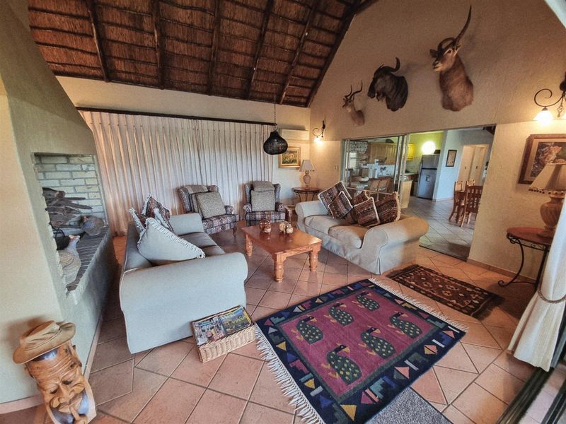 Spacious open-plan living area featuring a high vaulted thatched ceiling, built-in brick fireplace, and tiled flooring, with an adjacent kitchen and dining space.