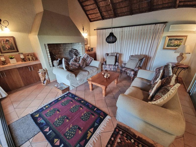 A cozy living room featuring a large built-in brick fireplace, terracotta floor tiles, and a high vaulted thatched ceiling.