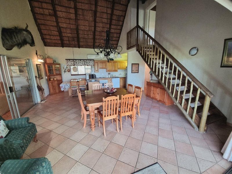 Open-plan living and dining area featuring a high thatched ceiling, tiled flooring, and a wooden staircase leading to the upper level.