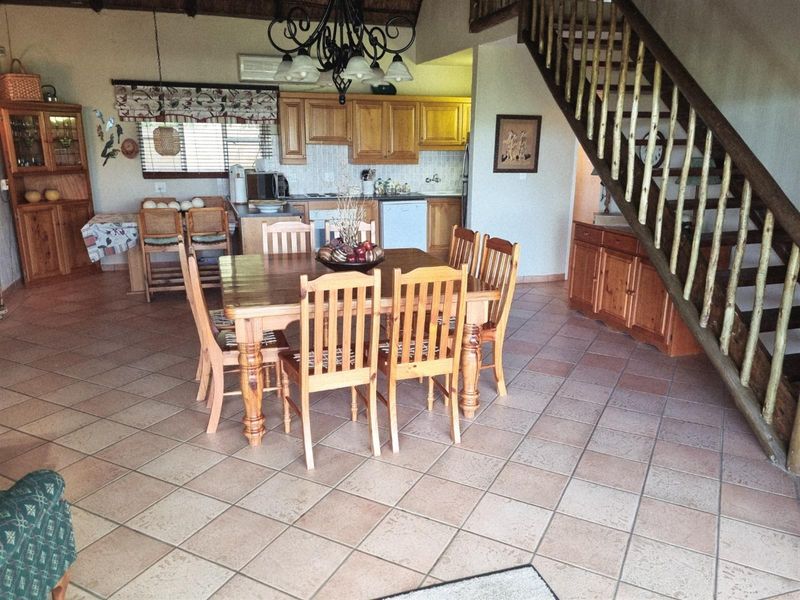 Open-plan living and dining area featuring tiled flooring, a wooden staircase, and a functional kitchen with built-in cabinetry.