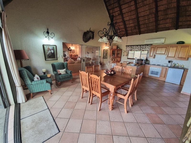 Open-plan living and dining area featuring a high thatched ceiling, tiled flooring, and a functional kitchen with wooden cabinetry.