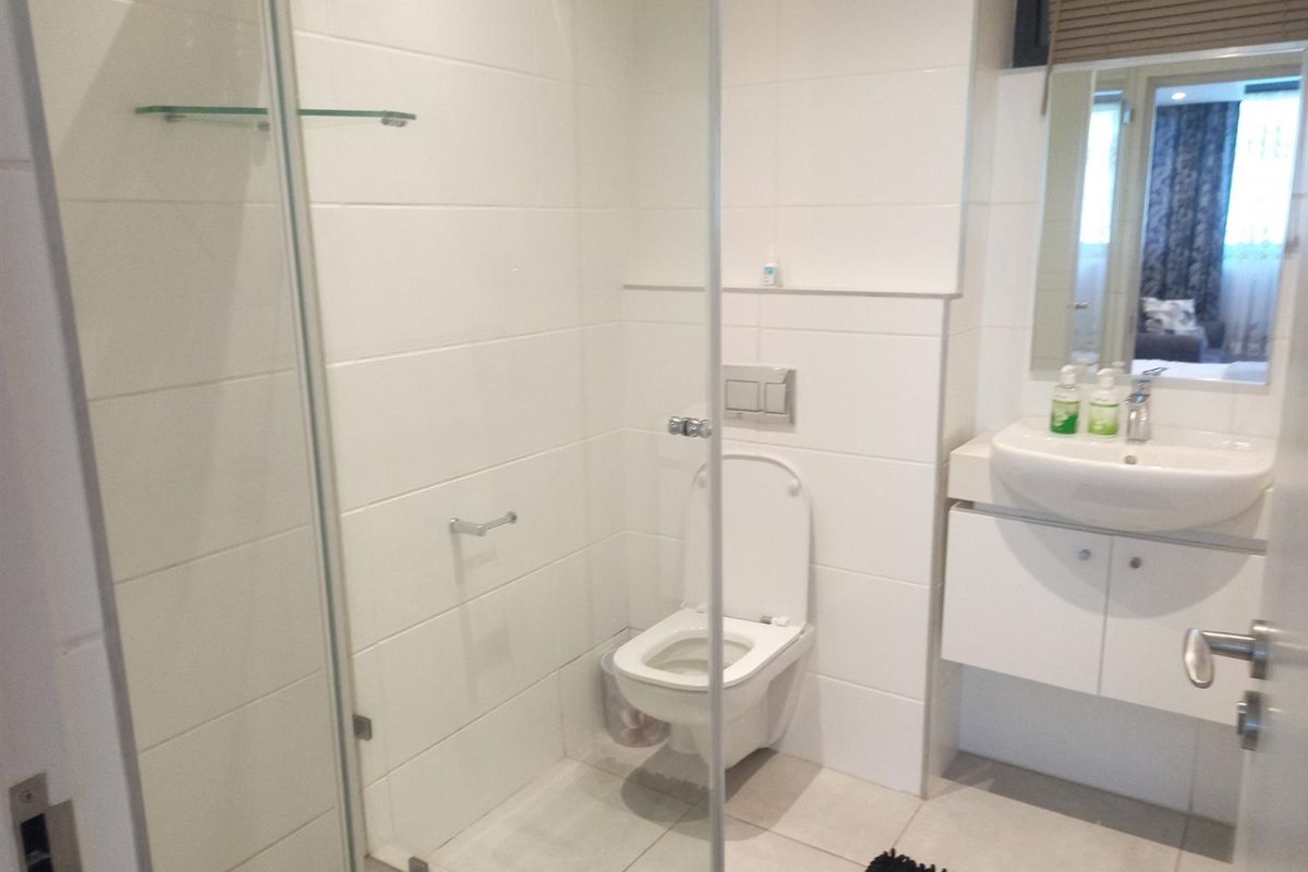 A modern bathroom featuring a glass-enclosed shower, wall-mounted toilet, and a vanity unit with a basin.