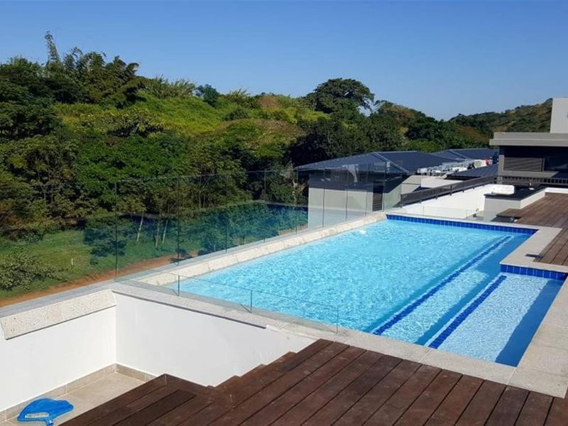 A rooftop swimming pool featuring a glass balustrade and timber decking, offering elevated views of the surrounding landscape.