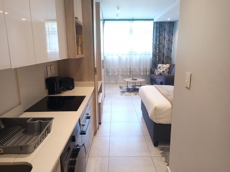 A modern open-plan studio apartment featuring a compact kitchen with built-in cabinetry, electric hob, and oven, flowing into a combined living and sleeping area.