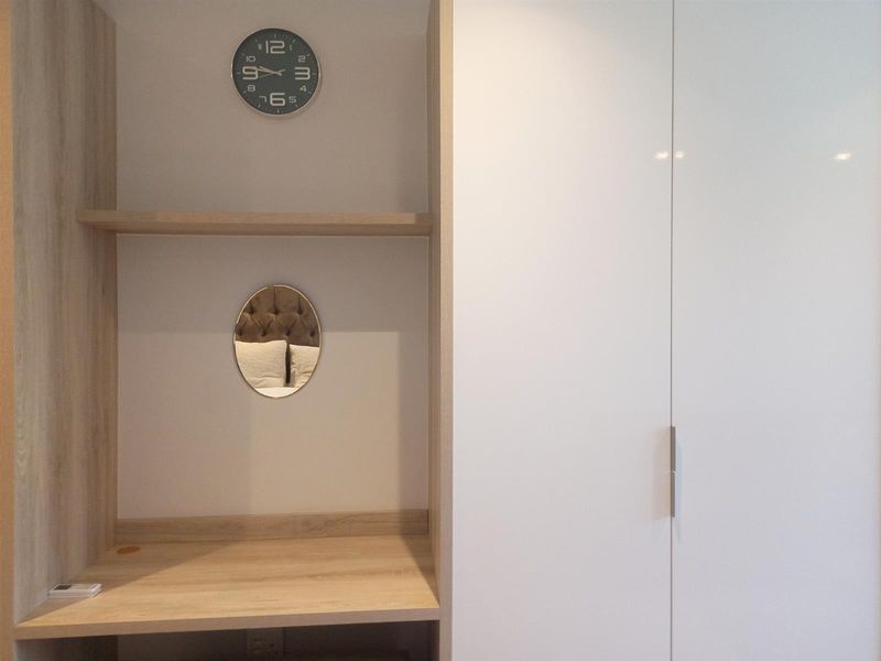 A built-in bedroom wardrobe unit featuring a light wood-tone desk area with shelving and a sleek white cabinet door finish.