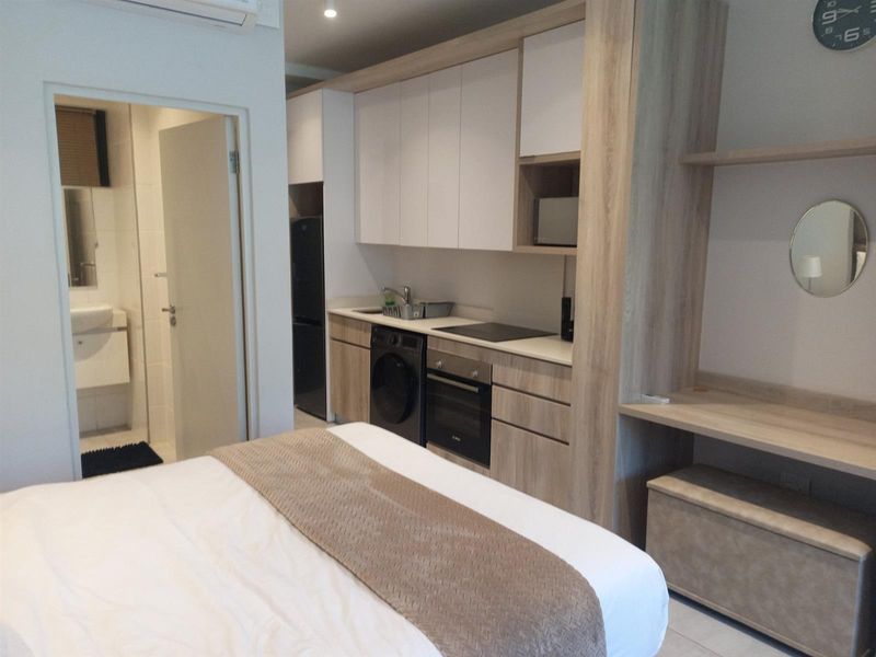 Compact studio apartment featuring a modern kitchenette with built-in cabinetry, integrated oven and hob, and an adjacent bathroom with a vanity.