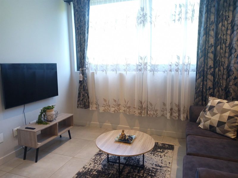 A cozy living room featuring tiled flooring and a large window with curtains, providing natural light to the space.