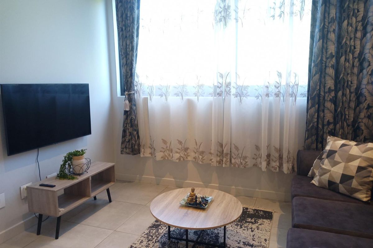 A cozy living room featuring tiled flooring and a large window with curtains, providing natural light to the space.