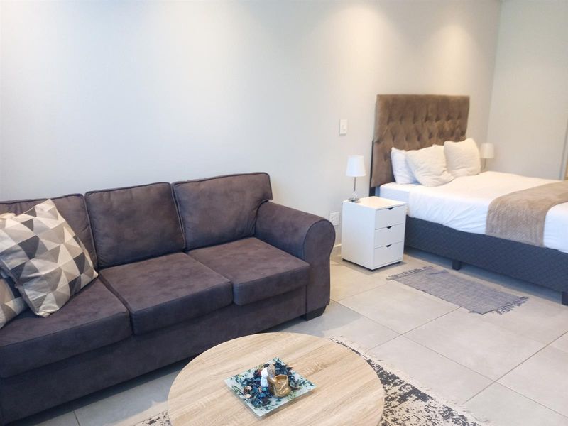 A studio apartment layout featuring a combined living and sleeping area with neutral tiled flooring and recessed ceiling lighting.
