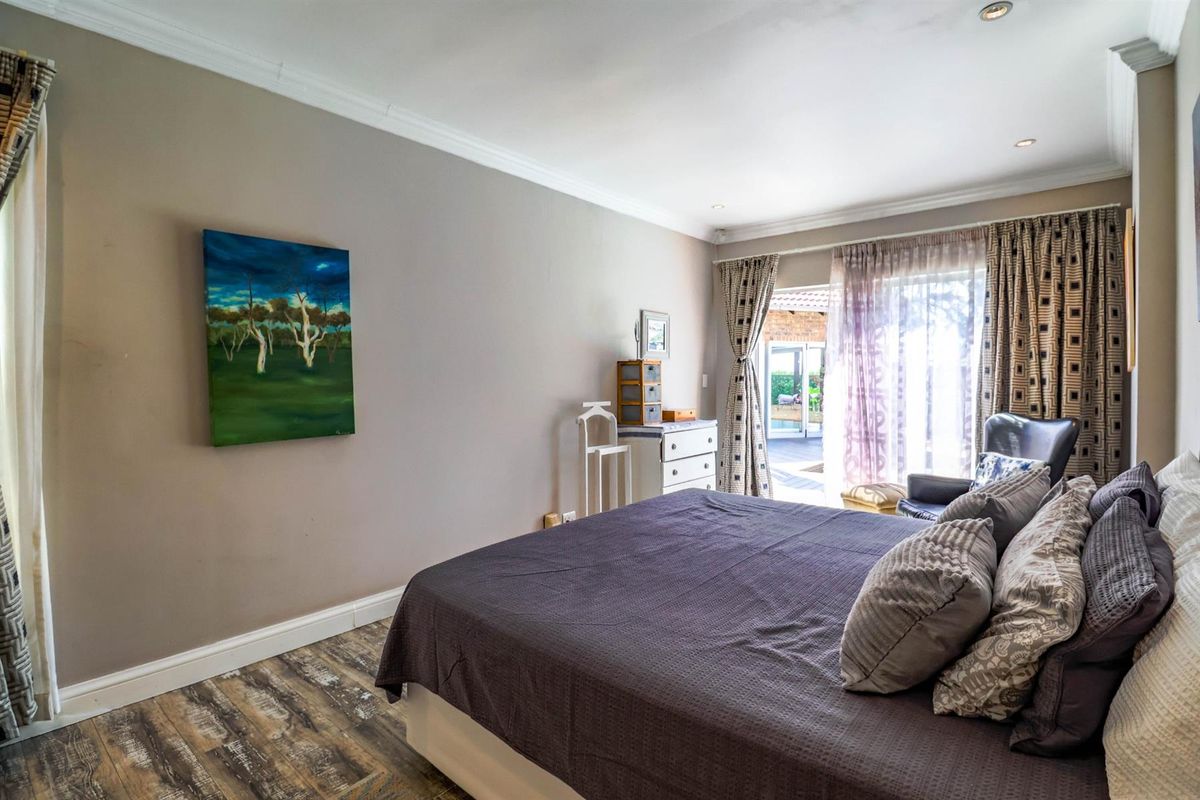 A well-maintained bedroom featuring wood-look flooring, crown molding, and direct access to an outdoor patio area through sliding glass doors.