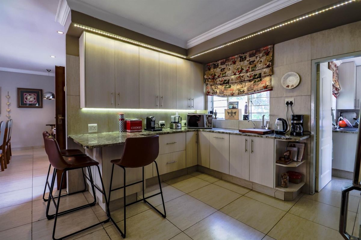 A modern kitchen featuring light-toned cabinetry, granite countertops, integrated LED under-cabinet lighting, and tiled flooring, with an adjacent breakfast bar area.