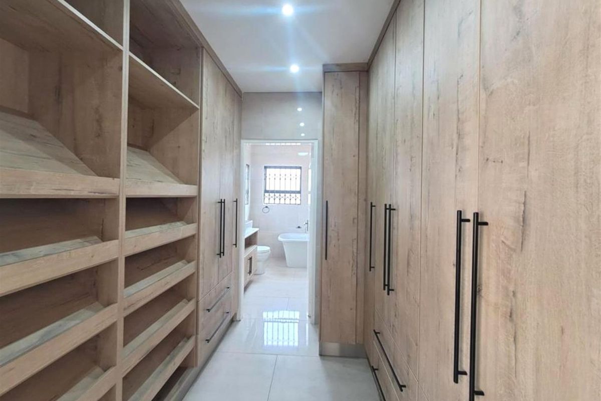 A modern walk-in dressing room featuring extensive built-in timber-look cabinetry with sleek black handles, leading directly into a bright, tiled en-suite bathroom.