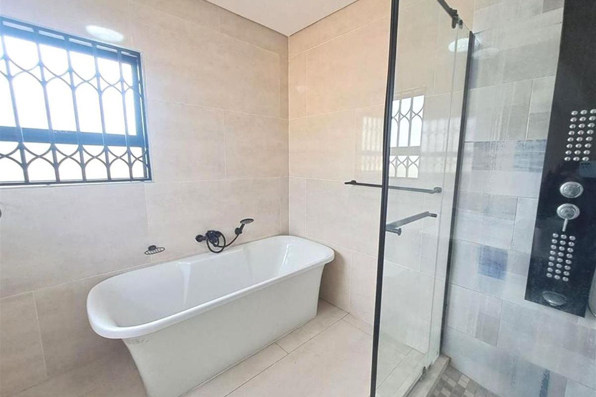 Modern bathroom featuring a freestanding bathtub, a glass-enclosed shower with a wall-mounted panel, and neutral floor-to-ceiling tiling.