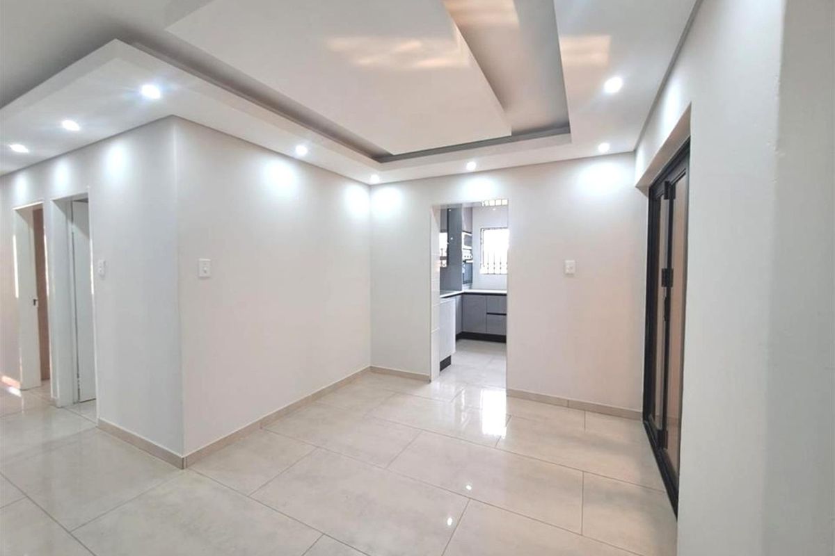 A bright, modern living area featuring a contemporary recessed ceiling with downlights, neutral tiled flooring, and a sliding glass door leading to the exterior.