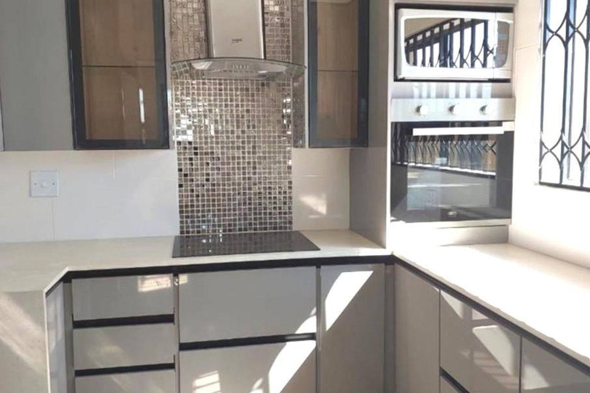 Modern kitchen featuring sleek grey cabinetry, stone countertops, mosaic tile backsplash, and integrated appliances including an oven, microwave, and extractor fan.