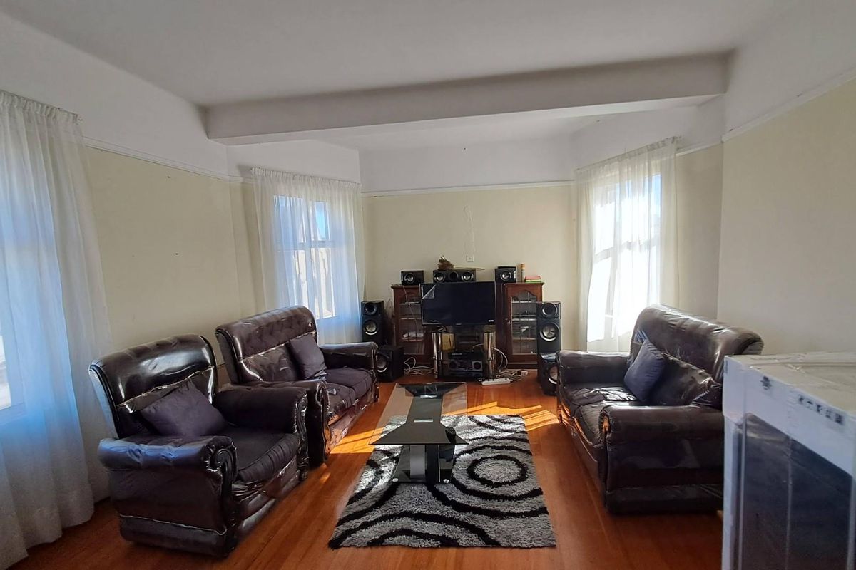 A spacious living room featuring polished hardwood flooring, a classic picture rail, and large bay windows that provide ample natural light.