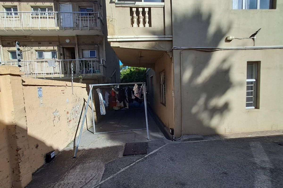 Rear exterior view of the apartment building showing a paved service area, boundary wall, and building facade with visible wear.