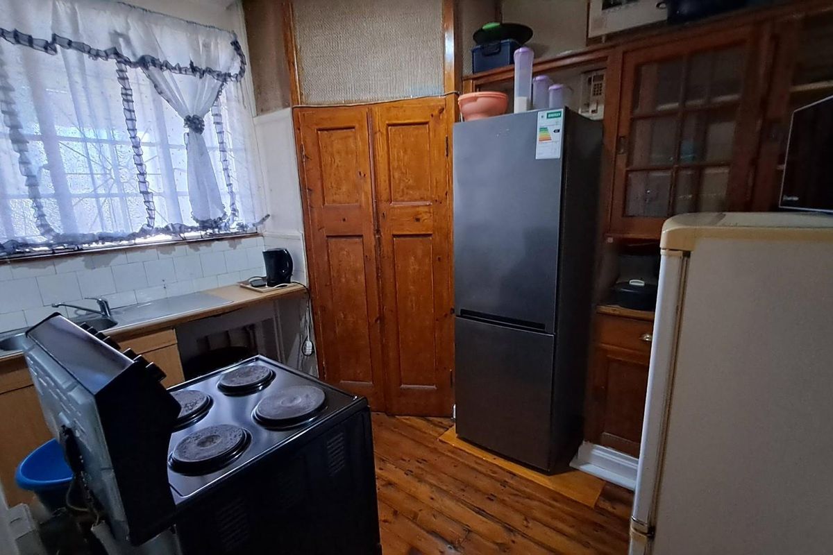 A dated kitchen featuring wooden cabinetry, a stainless steel sink, and an electric stove, with visible wear on the flooring and wall finishes.