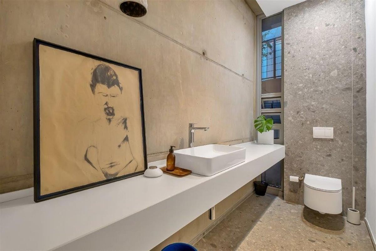 Modern bathroom featuring a floating vanity with a vessel sink, wall-mounted toilet, and industrial-style exposed concrete walls with stone flooring.