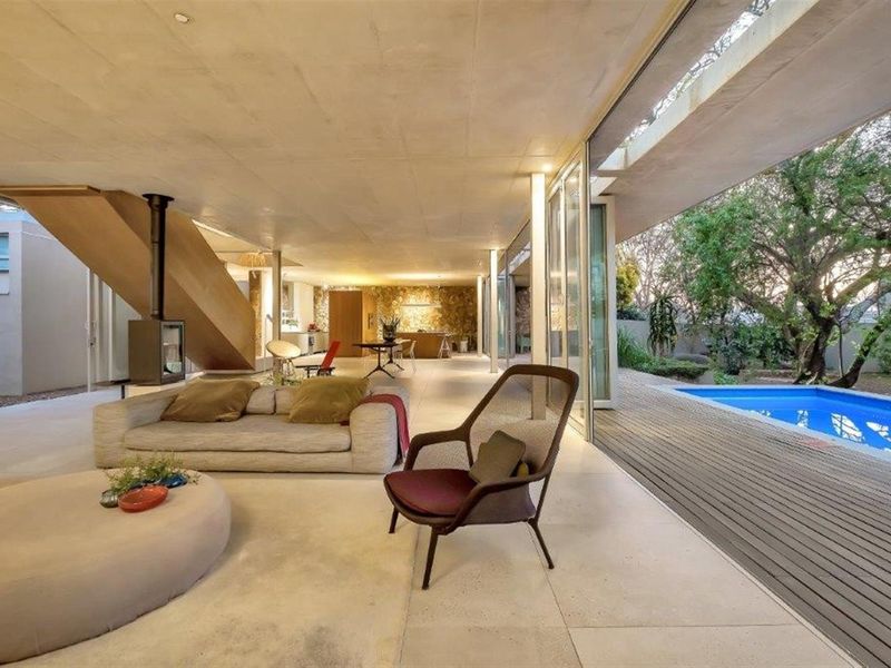 Spacious open-plan living area featuring a modern suspended fireplace, concrete ceiling, and seamless indoor-outdoor flow to a timber deck and swimming pool.