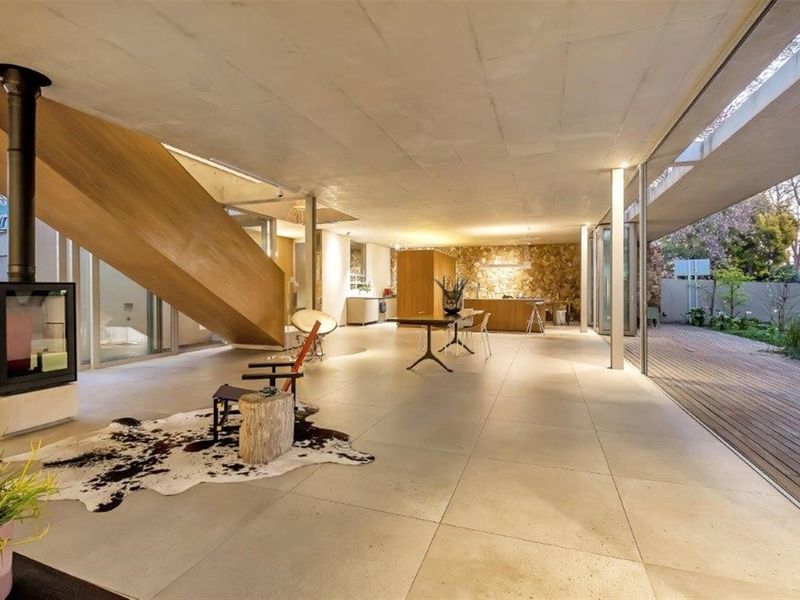 Spacious open-plan living area featuring large format floor tiles, a modern wood-burning fireplace, and seamless indoor-outdoor flow to a wooden deck.