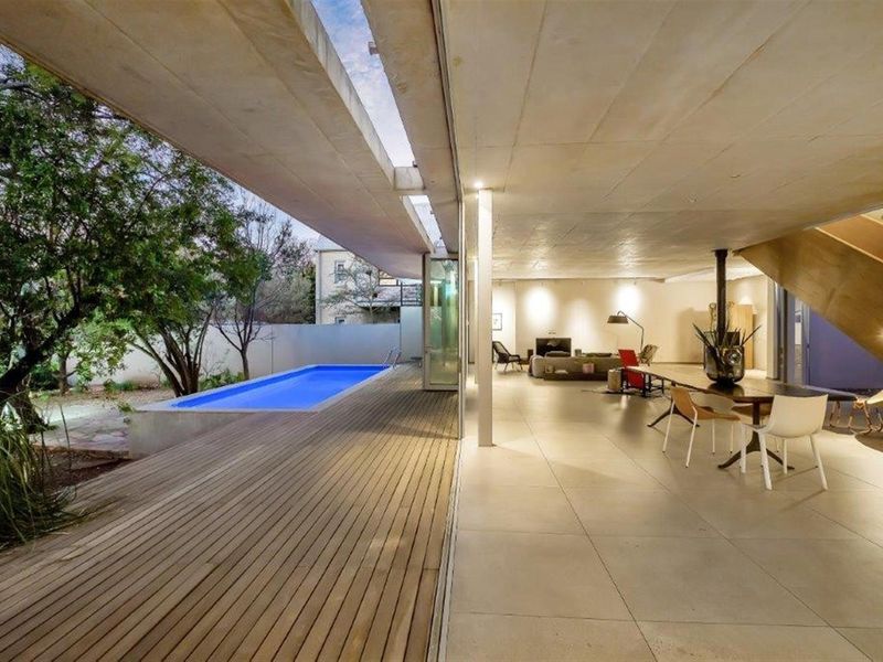 Spacious open-plan living area featuring large format floor tiles, a modern fireplace, and seamless indoor-outdoor flow to a timber deck and swimming pool.