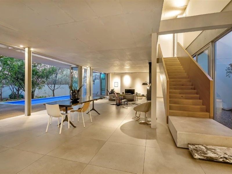 Spacious open-plan living area featuring polished concrete flooring, a modern timber staircase, and seamless indoor-outdoor flow to the pool deck.