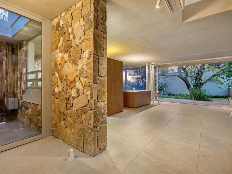 Modern open-plan living area featuring natural stone feature walls, large format floor tiles, and seamless indoor-outdoor flow through expansive glass sliding doors.