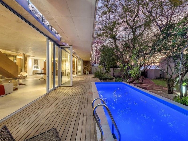 A modern outdoor patio featuring timber decking, a sleek lap pool, and seamless indoor-outdoor flow through large glass sliding doors.