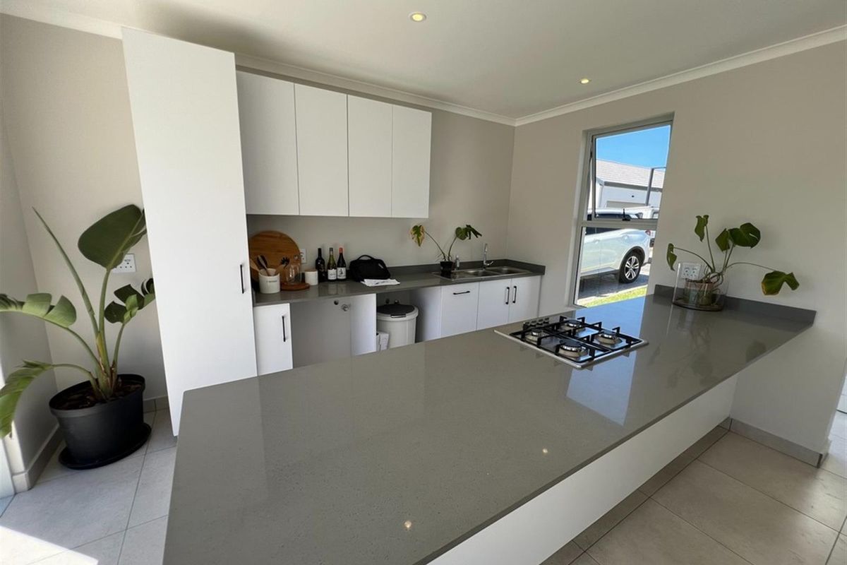 Modern kitchen featuring a large island with a built-in gas hob, stone countertops, and ample white cabinetry.