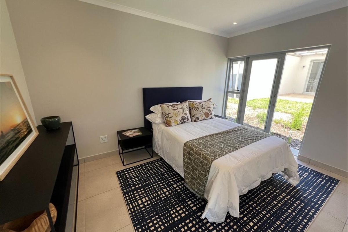 A bright bedroom featuring large sliding glass doors that provide direct access to an outdoor area, complemented by neutral tiled flooring.