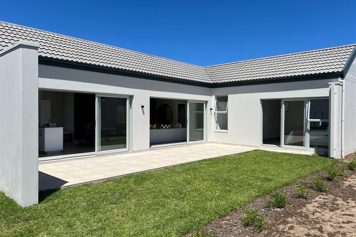 A modern rear exterior view featuring a tiled patio, large sliding glass doors, and a well-maintained lawn area.