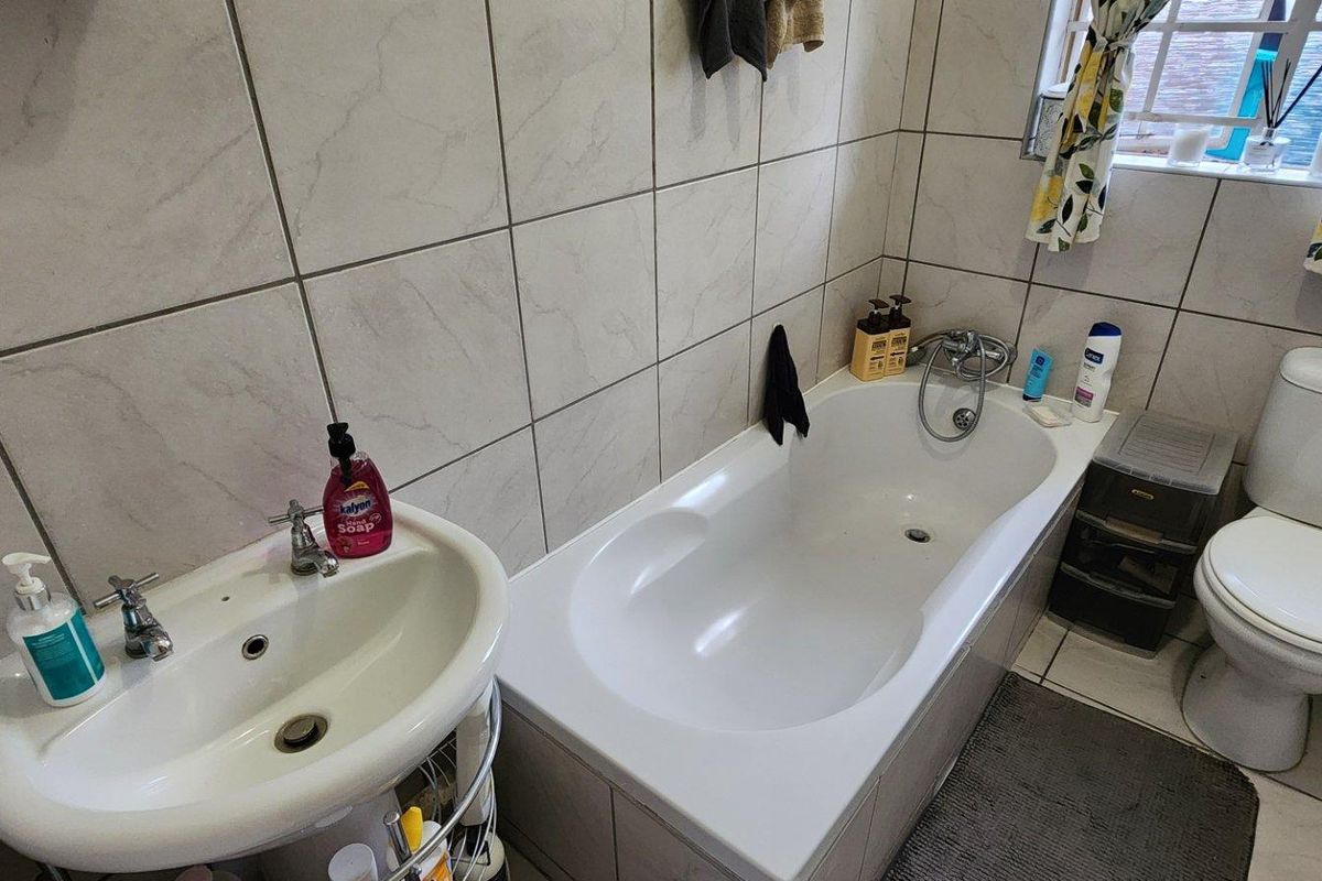 A functional bathroom featuring a bathtub, pedestal basin, and toilet with neutral wall tiling and natural light from a window.