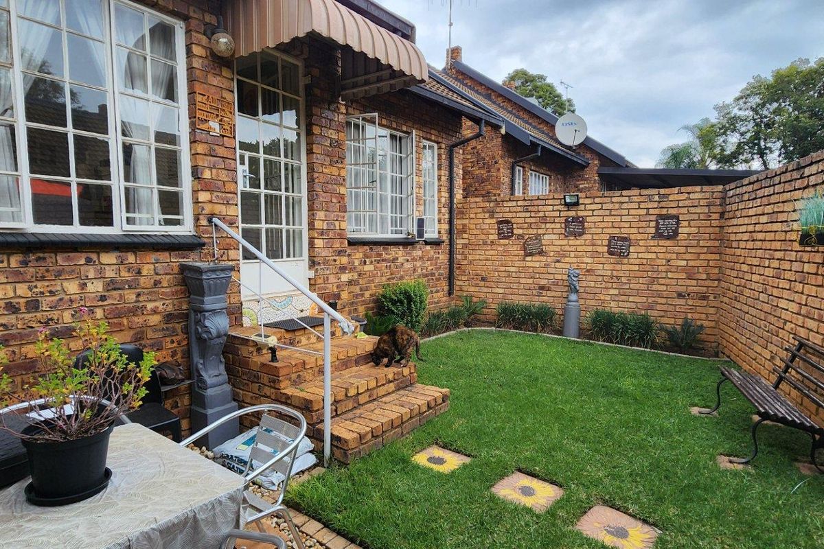 A private rear courtyard featuring a face brick townhouse facade, small lawn area, and secure boundary walling.