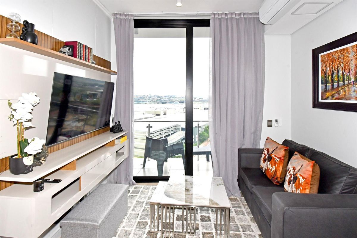 A modern living room featuring a built-in media console, split-system air conditioning, and direct access to a balcony with an urban view.