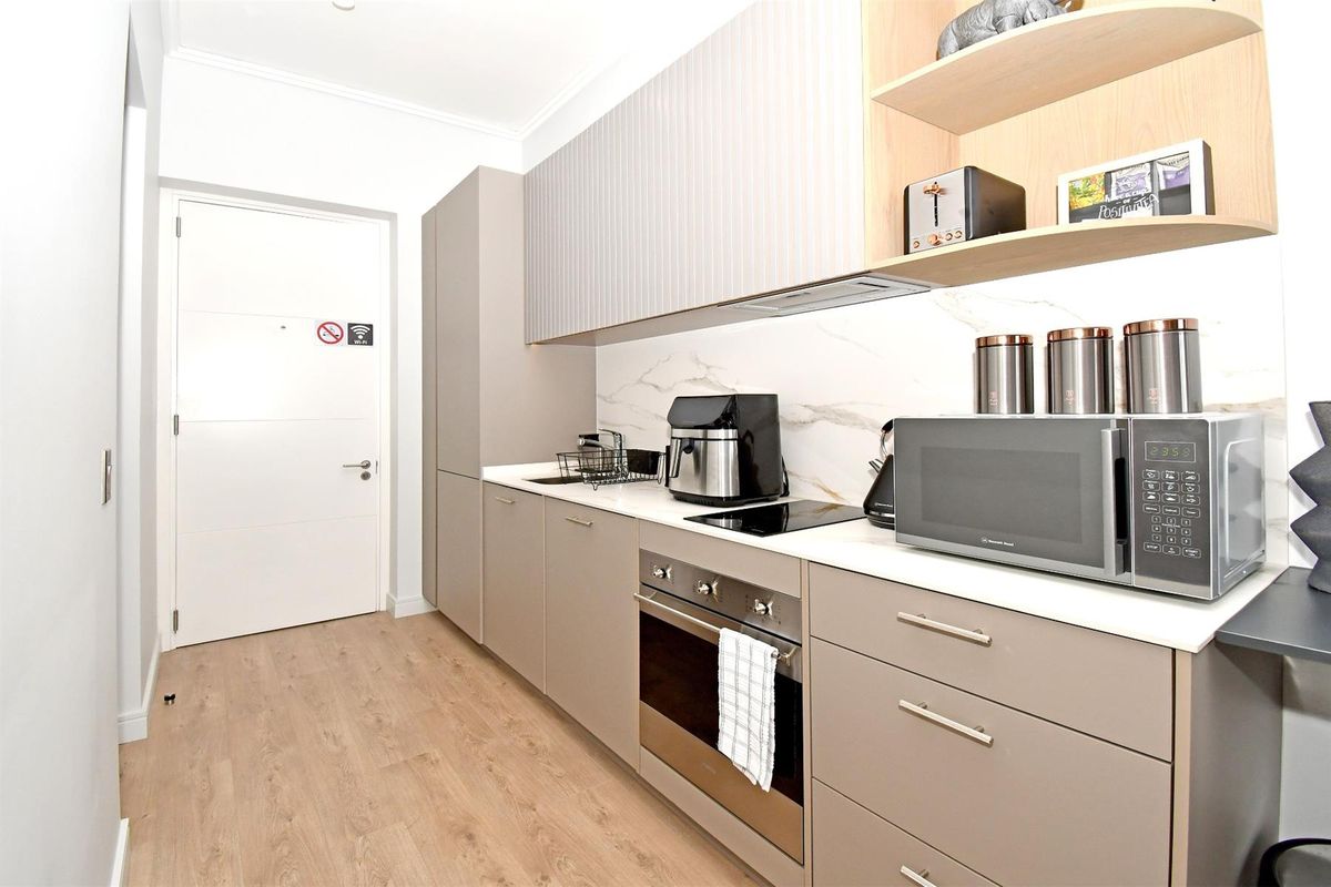 Modern galley-style kitchen featuring sleek taupe cabinetry, stone countertops, marble-look splashback, and integrated appliances, finished with light wood-look flooring.