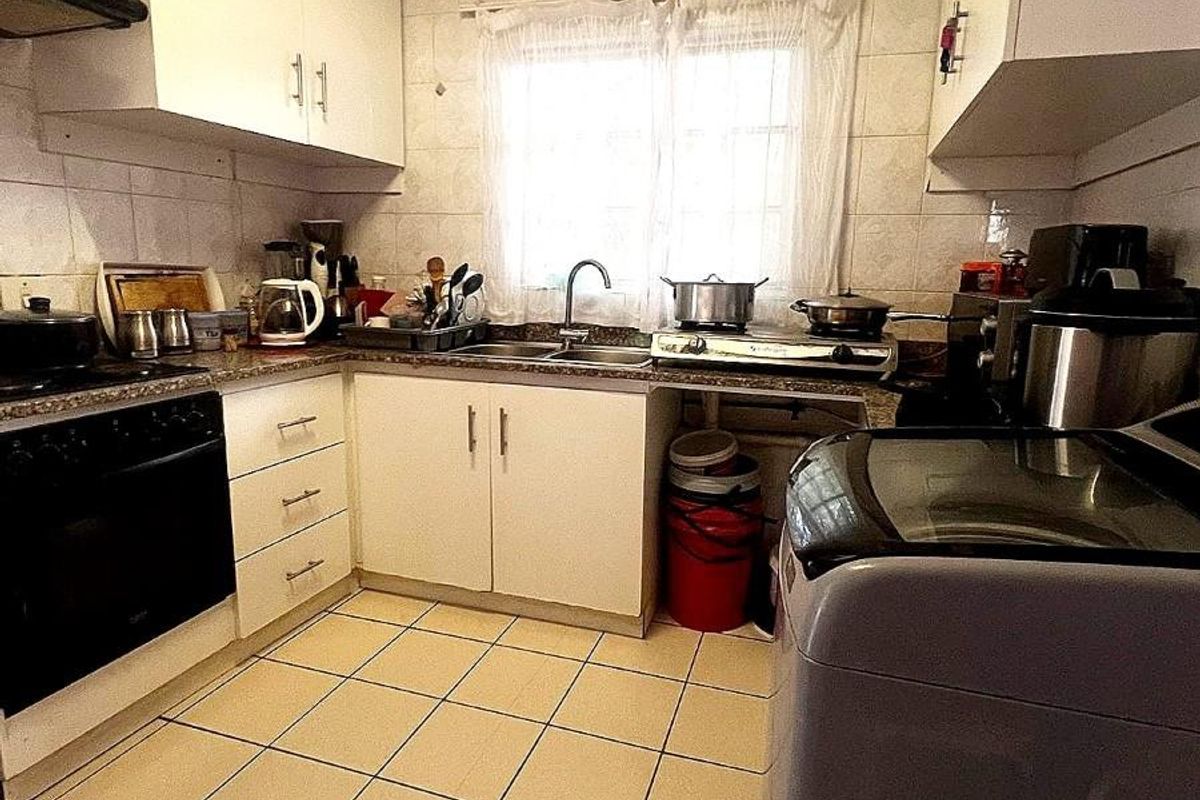 A compact kitchen featuring white cabinetry, tiled flooring, a built-in oven, and a double sink with tiled splashbacks.