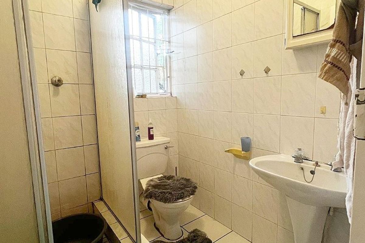 A compact bathroom featuring a pedestal basin, a standard toilet, and a shower enclosure with tiled walls and flooring.