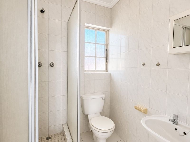 A clean, functional bathroom featuring a shower enclosure, pedestal basin, and toilet with neutral wall and floor tiling.