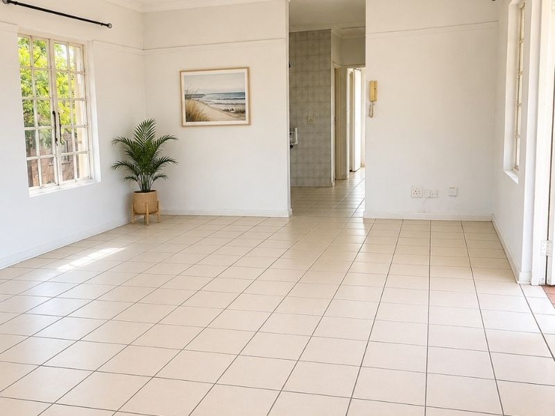 Spacious, light-filled living area featuring neutral ceramic floor tiles, a ceiling fan, and large windows, offering a clean canvas for personalization.