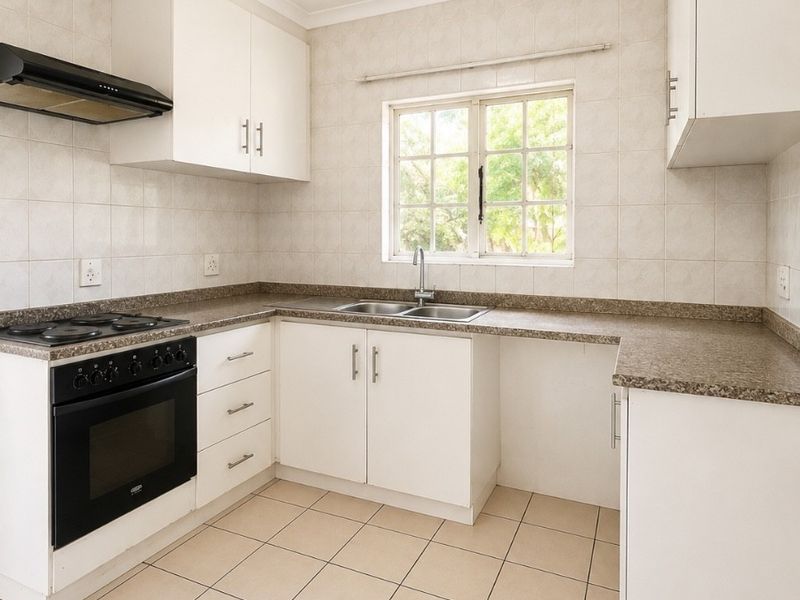 A clean, functional kitchen featuring white cabinetry, laminate countertops, a built-in oven with gas hob, and neutral ceramic floor tiles.