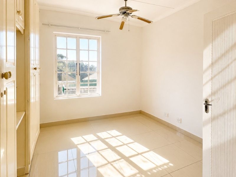 A bright, empty bedroom featuring neutral tiled flooring, built-in cupboards, and a ceiling fan, offering a clean and versatile living space.